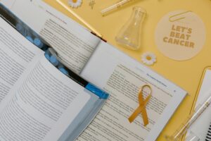 Open medical textbooks with a gold cancer awareness ribbon and “Let’s Beat Cancer” note on a yellow background.